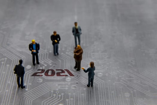 Miniature figurines posed as business people in a meeting over abstract futuristic circuit board with text year 2021