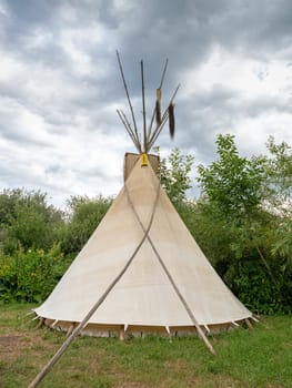 Back of a single Indian tipi stands in a meadow between trees and shrubs in the sunshine