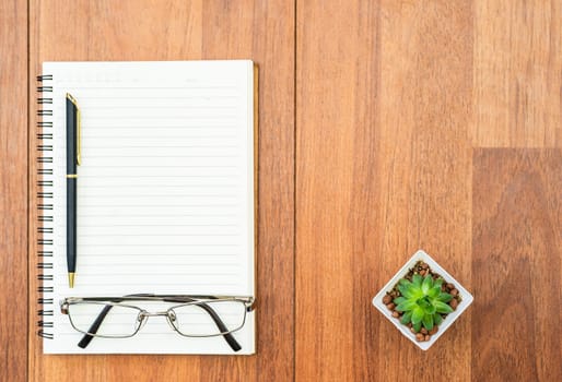 Top view eyeglasse and pen on notepad on wood deck with copyspace