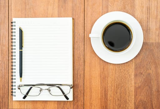 Top view eyeglasse and pen on notepad and coffee cup on wood deck