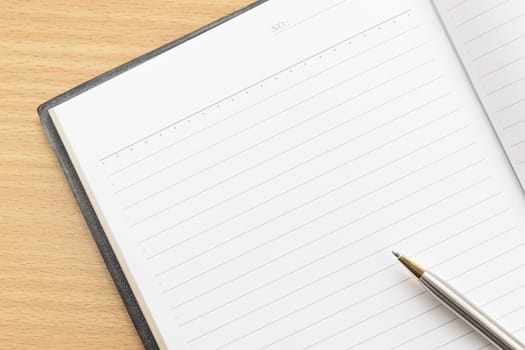 Pen and open notebook with blank page on wood table