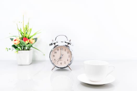 Silver alarm clock and coffee cup with flower on white background