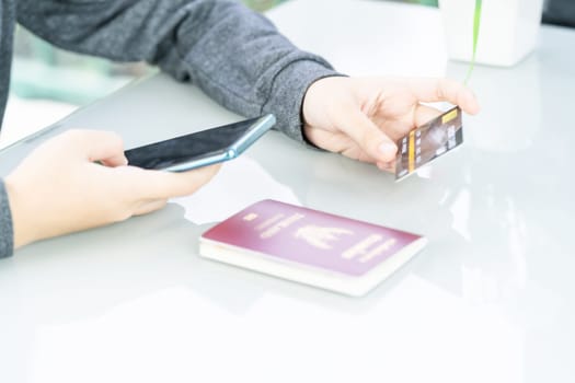 Woman holding credit card and passport using smartphone for online shoppingon deck in home office,Online shopping concept