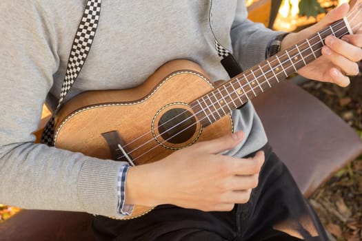 Young man sitting on bench in the park and playing ukulele.