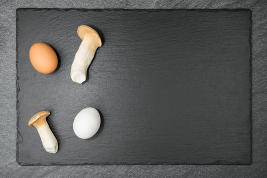 Two King Trumpet Mushrooms and a white and a brown egg on a slate slab. With copyspace. Flat lay.