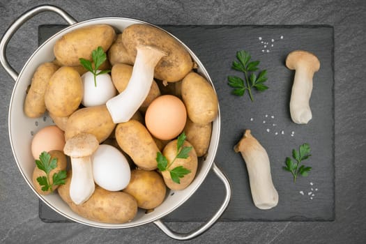 Two King Trumpet Mushrooms and a white and a brown egg on a slate slab with coarse salt grains. With copyspace. Flat lay.