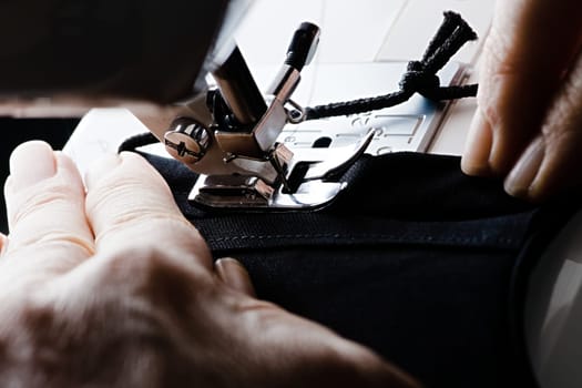 From right to left, a seam is stitched on a black homemade face covering or face mask. Guided by older weathered hands.