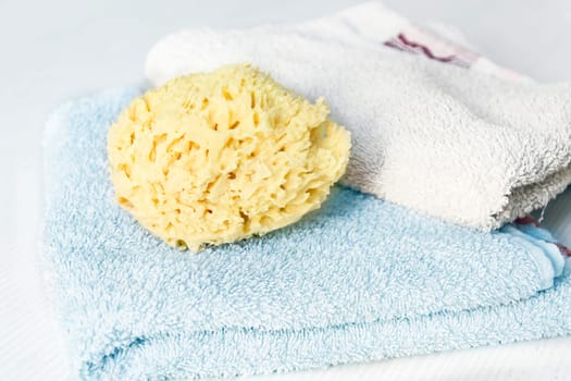 A natural yellow sponge on towels stacked on a white wooden table. Personal care and hygiene. Bath and relax