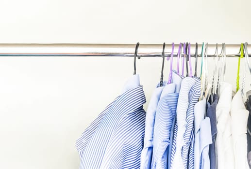 A group of men's shirts of various colors hung with hangers inside a wardrobe. Fashion and clothes.