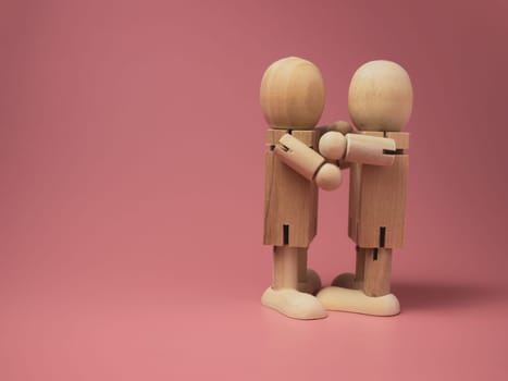 2 wooden dolls hugging each other on a pink background..Concept of social contact from wooden dolls.