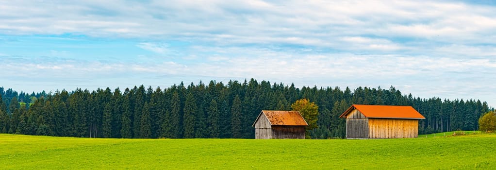Countryside farm in Bavaria, Germany, Europe. Winding road in foreground, blue cloudy sky in background. Barns with orange tiled roofs.