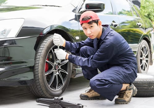 Young mechanic in uniform replacing lug nuts by hand while changing tires on a vehicle