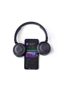 Lod, Israel - July 8, 2020: Black mobile smartphone with Smule app play store page and wireless headphones on a white background. Top view flat lay with copy space.