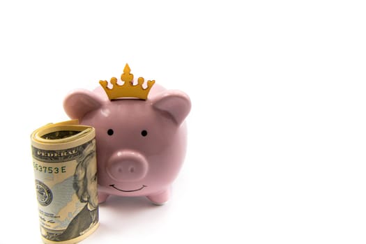Pink piggy bank with golden crown and stack of US dollars in front isolated over white background with copy space, cash is king concept image