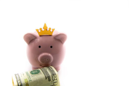 Pink piggy bank with golden crown and stack of US dollars in front isolated over white background with copy space, cash is king concept image