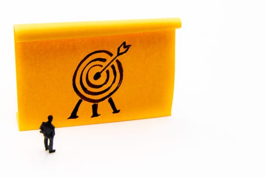 Miniature figurine posed as businessman in front of target hand drawn on adhesive paper note, performance concept image