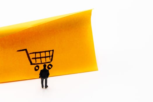 Miniature figurine posed as businessman looking at shopping cart handrawn on adhesive paper note, e-commerce concept image