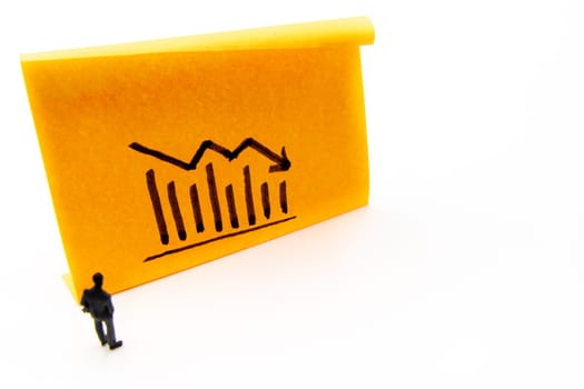 Miniature figurine posed as businessman in front of descending graph arrow hand drawn on adhesive paper note, negative performance concept image