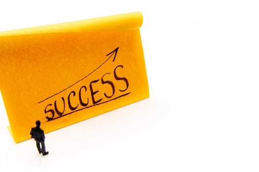 Miniature figurine posed as businessman on ascending graph arrow with Success growth text handwritten on adhesive paper note, positive performance concept image
