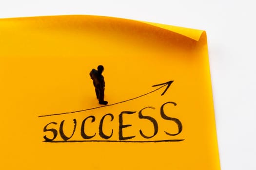 Miniature figurine posed as businessman on ascending graph arrow with Success growth text handwritten on adhesive paper note, positive performance concept image