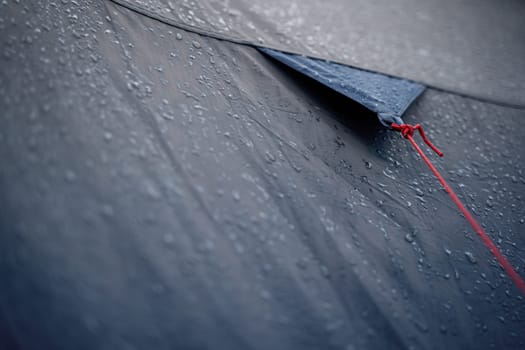 closeup detail perspective view of anchoring red rope on dark blue outdoor waterproof tent covered in rain drops
