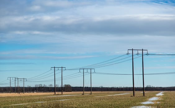 Electricity Pylons in Thawing Field in spring with clouds above.