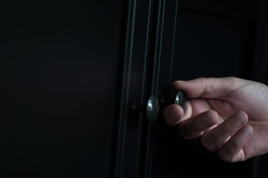 perspective side view closeup of Caucasian man hand opening a wooden closed black clothes dresser cabinet with a metallic door knob