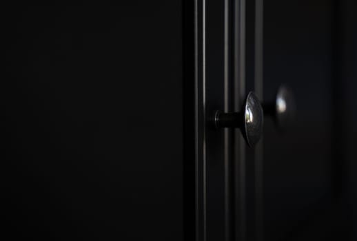 perspective side view closeup of two metallic door knobs on wooden closed black clothes dresser cabinet