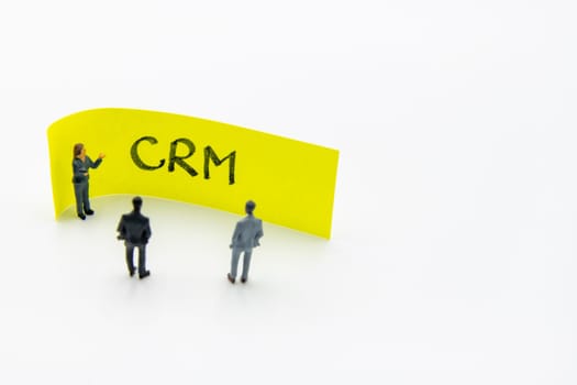 Presentation meeting with miniature figurines posed as business people standing in front of post-it note with CRM Customer Relationship Management handwritten message in background