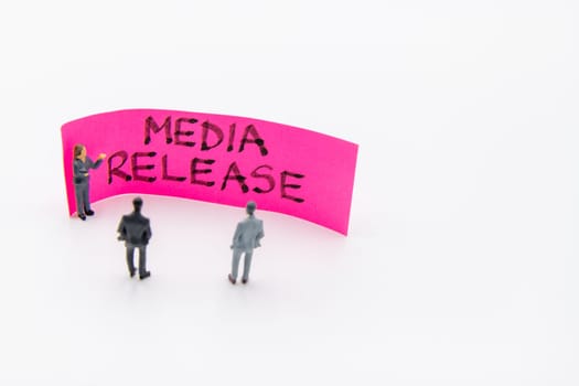 Presentation meeting with miniature figurines posed as business people standing in front of post-it note with Media Release handwritten message in background, copy space on the right