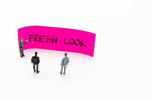 Presentation meeting with miniature figurines posed as business people standing in front of post-it note with Fresh Look handwritten message in background, copy space on the right