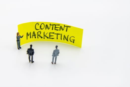 Presentation meeting with miniature figurines posed as business people standing in front of post-it note with Content Marketing handwritten message in background, copy space on the right