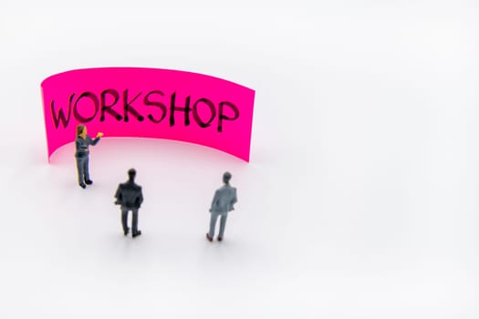 Presentation meeting with miniature figurines posed as business people standing in front of post-it note with Workshop handwritten message in background, copy space on the right