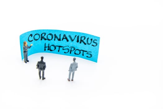 Presentation meeting with miniature figurines posed as business people standing in front of post-it note with Coronavirus Hotspots handwritten message in background, copy space on the right