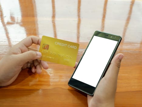 Online shopping concept with human hand holding smart phone and credit card on wood table background.