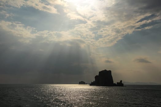 Sun rays shining on small deserted island in Andaman sea near Phi Phi, showing only silhouette of rock. Ao Nang, Thailand