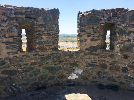 Ancient stone battlements and loopholes with view of countryside and distant horizon under blue sky in natural light. Full frame of rough stone texture and gentle nature with copy space.
