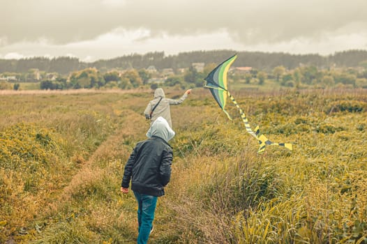 mom and son teenager in warm clothes run across the field, launching a kite