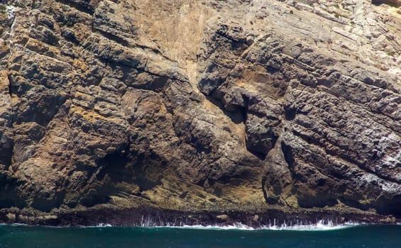 gorgeous massive cliff with ocean waves crashing its base. Beautiful colors and texture.