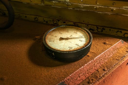 Old industrial circular thermometer gauge showing high temperature, on top of oven used to dry tea, covered with brown tea dust.