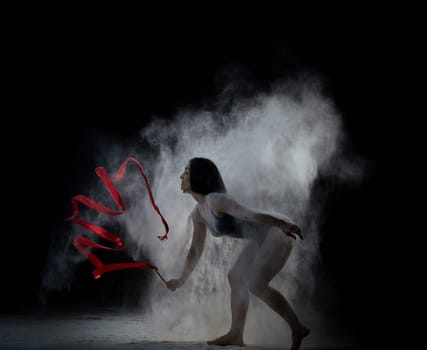 beautiful caucasian woman in a black bodysuit with a sports figure dancing with red ribbon on a black background, explosion and expression in motion