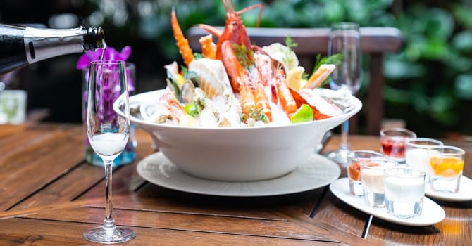 Waiter pouring white wine into wine glass and serving to customer in restaurant with big bowl seafood on ice in background. Restaurant gastronomy food and drink consumerism concept.