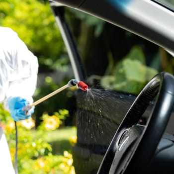 Close up of chemical alcohol spray cleaning inside car to disinfect and decontaminate coronavirus covid-19 by specialist cleaner wearing personal protective equipment PPE. New normal Hygiene concept.