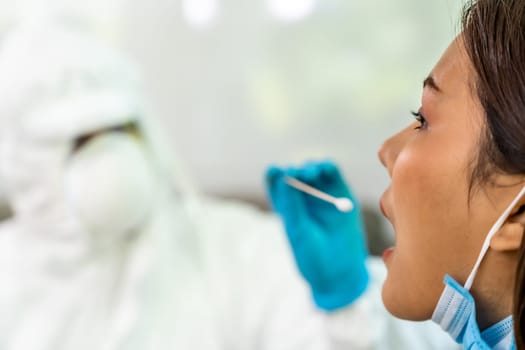 Medical staff with PPE suit test coronavirus covid-19 to asian woman by throat swab at home. New normal health care service at home and medical delivery and COVID-19 testing concept.