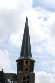 Steeple with a cross and clock, a blue sky in the background.