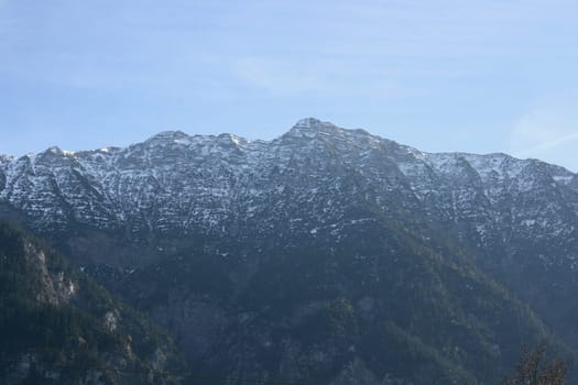 Alpine summits covered with snow, blue sky in the background .