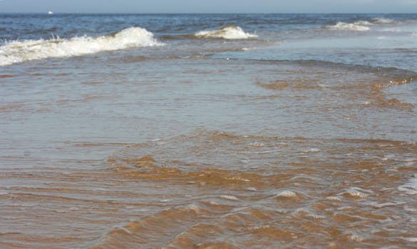 Waves with whitecaps flood the sandy beach.