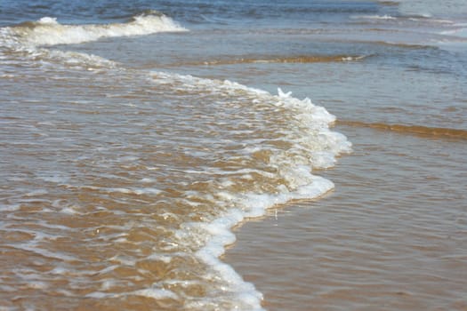 Waves with whitecaps flood the sandy beach.