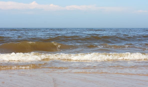 Waves with whitecaps flood the sandy beach.