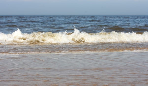 Waves with whitecaps flood the sandy beach.